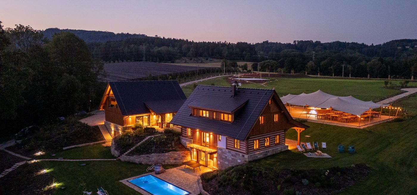 Resort Na Pasece za soumraku z dronu, rozsvícené roubenky, bazén a stany
